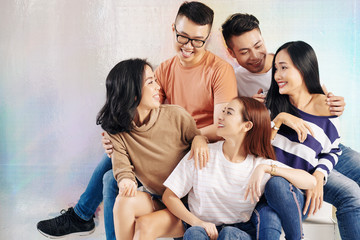 Cheerful smiling young Asian men and women sitting in studio and looking at each other