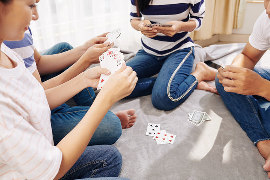 Cropped image of friends sitting on the floor and playing cards