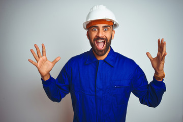 Handsome indian worker man wearing uniform and helmet over isolated white background celebrating...