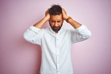 Young indian businessman wearing elegant shirt standing over isolated pink background suffering from headache desperate and stressed because pain and migraine. Hands on head.