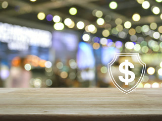 Dollar with shield flat icon on wooden table over blur light and shadow of shopping mall, Business money insurance and protection concept