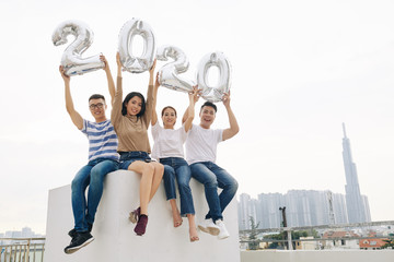 Joyful excited young Asian people sitting on rooftop and showing balloon figures