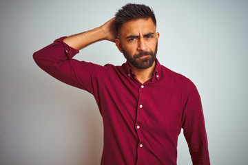 Young indian man wearing red elegant shirt standing over isolated grey background confuse and wondering about question. Uncertain with doubt, thinking with hand on head. Pensive concept.