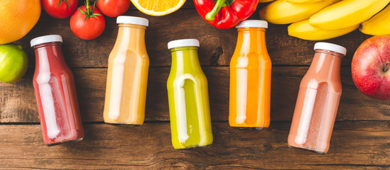 Multicoloured juices in bottles on old wooden background with fruits and vegetables. Top view....