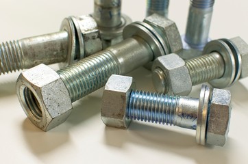 Stainless steel nuts and bolts on white background with strong defocus