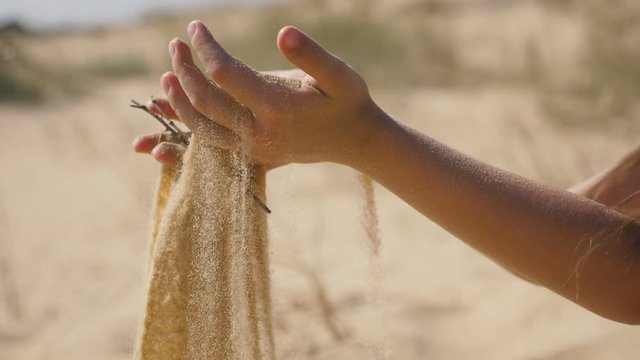 Female hands raising sand in a handfull on a sea beach on a sunny day in slo-mo