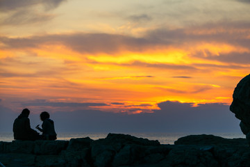 couple sitting on rocky cliff looking on sunset. romantic date