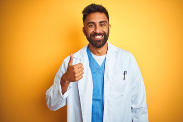 Young indian doctor man standing over isolated yellow background doing happy thumbs up gesture with...