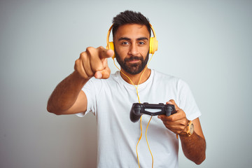 Arab indian gamer man playing video game using headphones over isolated white background pointing with finger to the camera and to you, hand sign, positive and confident gesture from the front