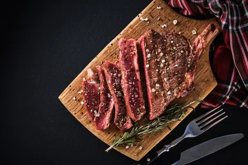Gartenposter Entrecote. Steak am Knochen. Rib-Eye. Tomahawk-Steak auf einem Schneidebrett mit Rosmarin. Braten - Selten © FoodAndPhoto