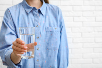 Woman holding glass of water near brick wall, closeup with space for text. Refreshing drink