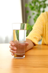 Woman holding glass of water at wooden table, closeup. Refreshing drink