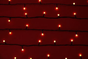 Glowing Christmas lights on red background, top view