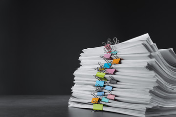 Stack of documents with binder clips on grey stone table against black background, space for text