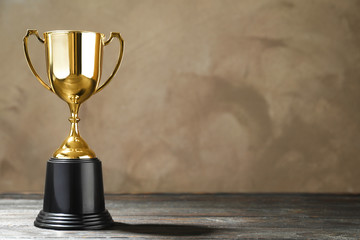 Golden trophy cup on wooden table against light brown background. Space for text
