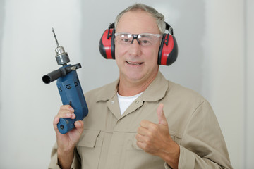 portrait of cheerful man builder with drill showing thumb-up