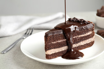 Pouring chocolate sauce onto delicious fresh cake on light table, closeup