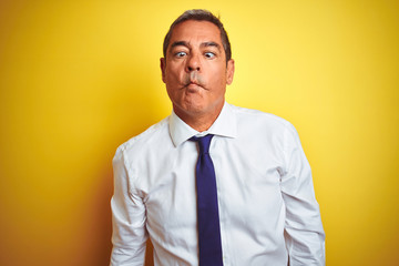 Handsome middle age businessman standing over isolated yellow background making fish face with lips, crazy and comical gesture. Funny expression.