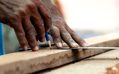 Close-up of a carpenter's hand, using a ruler and a pencil to make wood