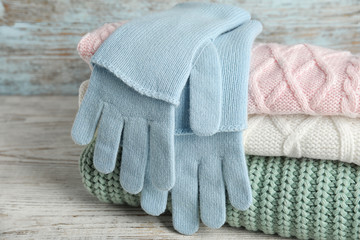 Stacked sweaters and gloves on wooden table, closeup. Autumn clothes