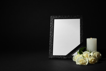 Funeral photo frame with ribbon, white roses and candle on dark table against black background....