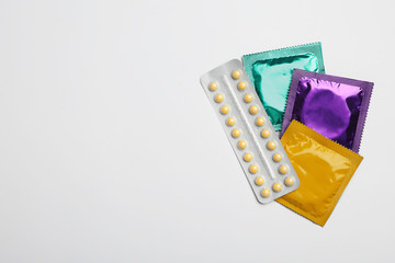 Condoms and birth control pills on light grey background, flat lay with space for text. Safe sex...