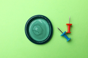 Blue condom and pin on green background, flat lay