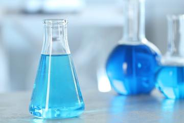 Conical flask with light blue liquid on table in laboratory. Space for text