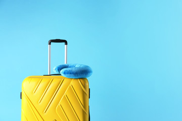 Yellow suitcase and travel pillow on light blue background, space for text