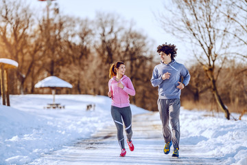Fototapeta na wymiar Happy smiling caucasian couple in sportswear running in nature while looking at each other. Winter time.
