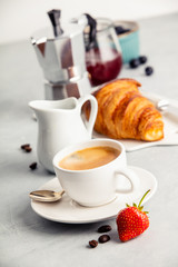 Coffee espresso in white cup with milk, jam and croissants.