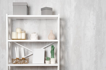 Fototapeta na wymiar Wooden shelving unit with decor near grey wall. Bookcase with photo frame mockup and candles, living room interior details