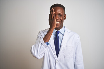 Young african american doctor man wearing coat standing over isolated white background covering one eye with hand, confident smile on face and surprise emotion.