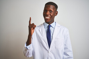 Young african american doctor man wearing coat standing over isolated white background pointing finger up with successful idea. Exited and happy. Number one.