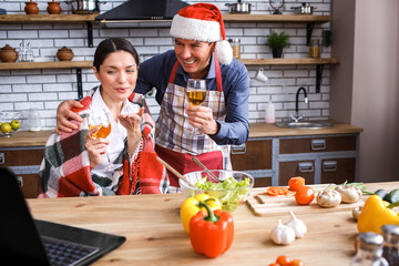 Happy festive man and woman in kitchen. Holding wine glasses in hands and smile. Celebrating new...