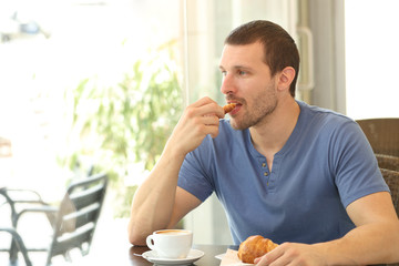 Relaxed man eating a croissant in a coffee shop