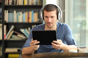 Serious man using tablet and headphones in a coffee shop