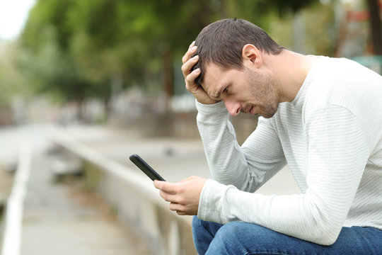 Sad adult man checking bad news on smart phone