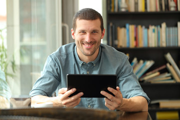 Happy man holding tablet looking at camera in a bar