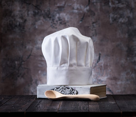 Chef hat, cookbook and wooden spoons on a wooden table..Cooking still life