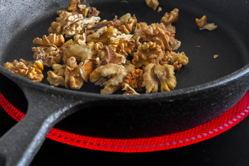 Walnuts cooking in a cast iron frying pan on a ceramic hob stove