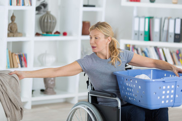 woman in wheelchair holding basket and picking up laundry