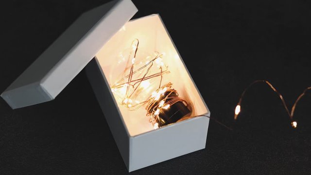 thinking outside the box, idea lightbulb wrapped up in string lights shining from open box