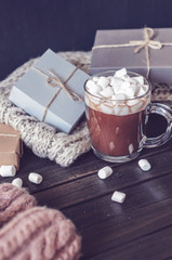 Hot cocoa with marshmallows in a glass cup surrounded by Christmas gifts and winter clothes, Christmas atmosphere and coziness