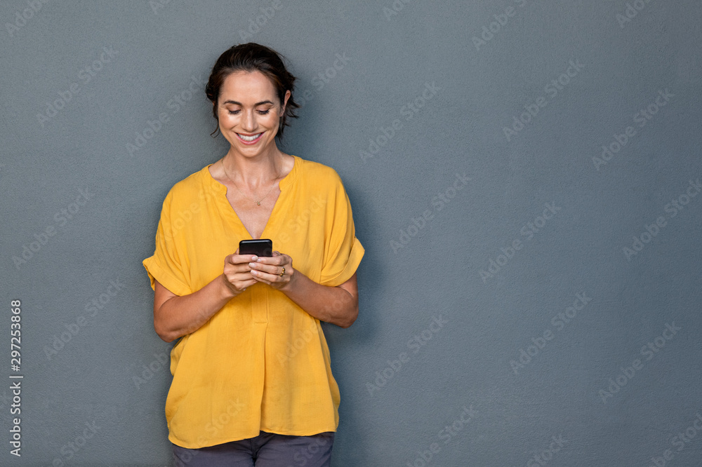 Wall mural mature latin woman using smart phone on gray wall