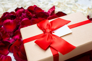 Gift box with dark red and white rose petals on white wooden background. Valentine's background.