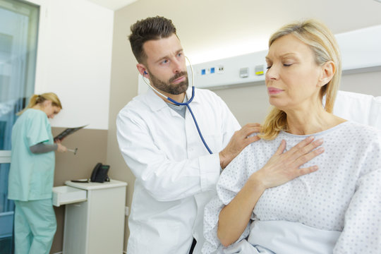 doctor monitoring mature female patient with chest pain
