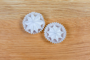 Meringue cookies in paper molds on wooden surface, top view