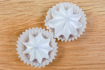 Meringue cookies in paper molds on wooden surface, top view