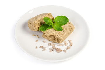 Pieces of sunflower halva, mint, sunflower seeds on white dish